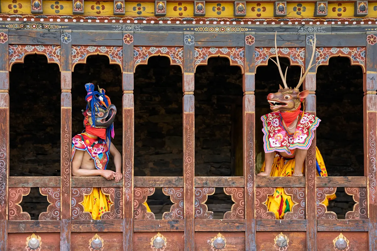 Mask dancers performing in front of a monastery window during a Bhutanese Tshechu festival